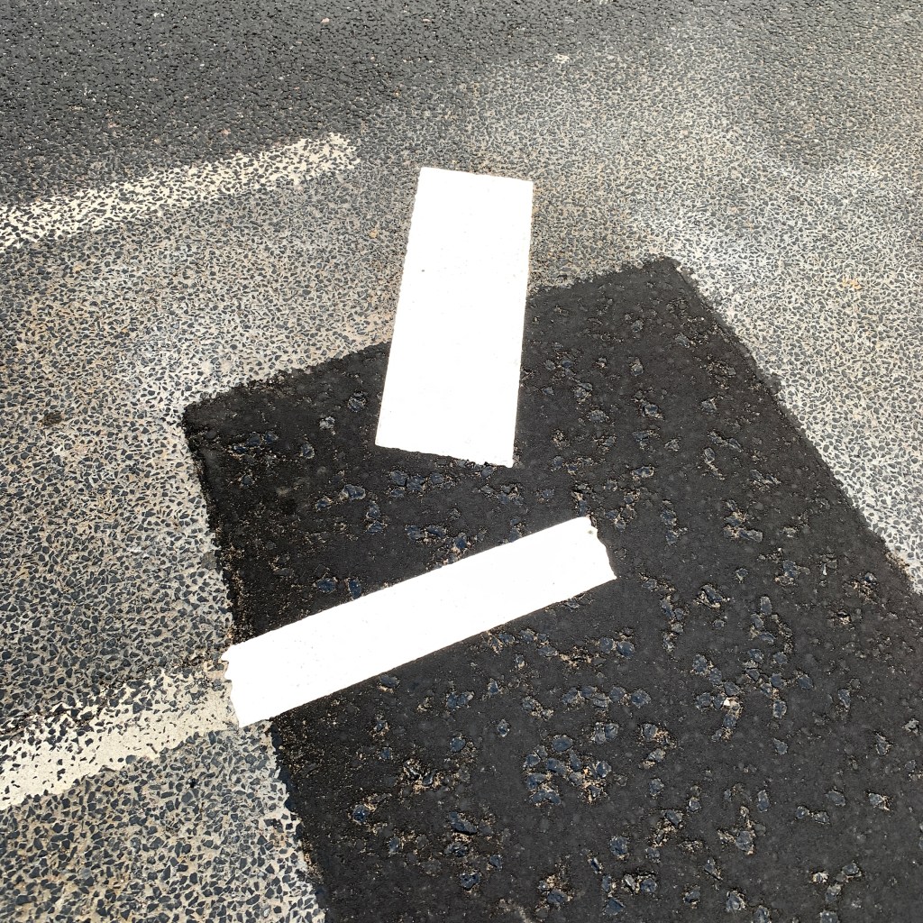 A photograph of repainted white street markings on a tarmac surface.