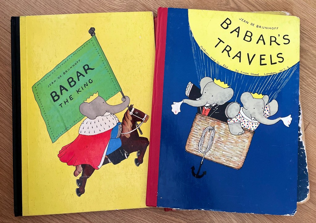 A photograph of the front of 2 Babar the Elephant picture books. The left hand book features an illustration of Babar on a horse with a flag in its trunk, and the right hand image features Babar and wife Celeste in the basket of a hot air balloon.