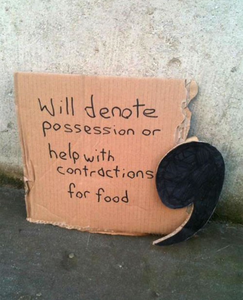 A photograph of a piece of ripped cardboard with text written on it in marker pen and a cardboard apostrophe propped up by its right hand side.