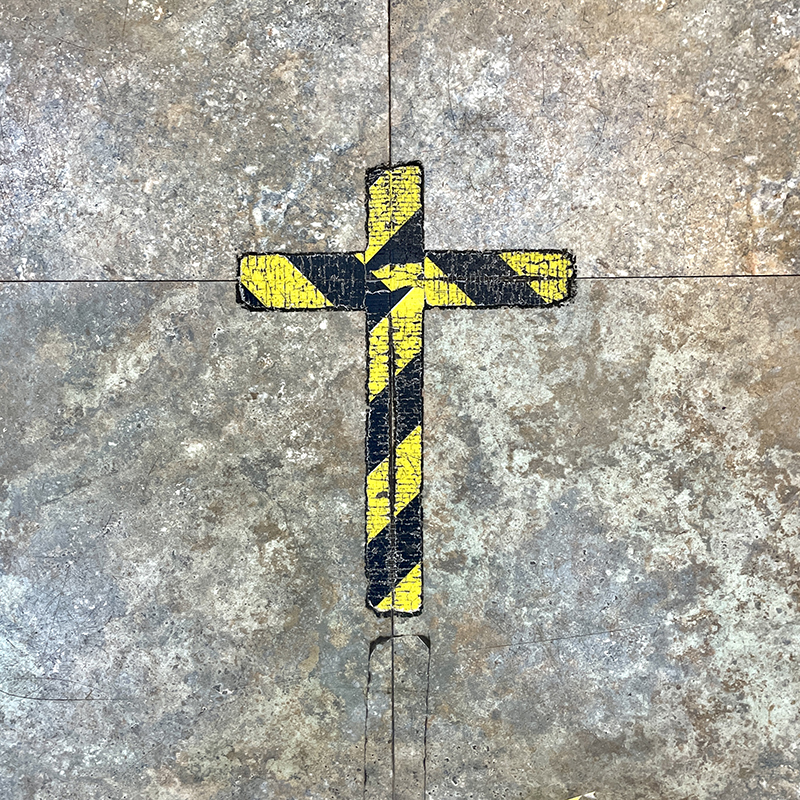 Yellow and black striped tape in the form of a cross stuck to a tiled floor