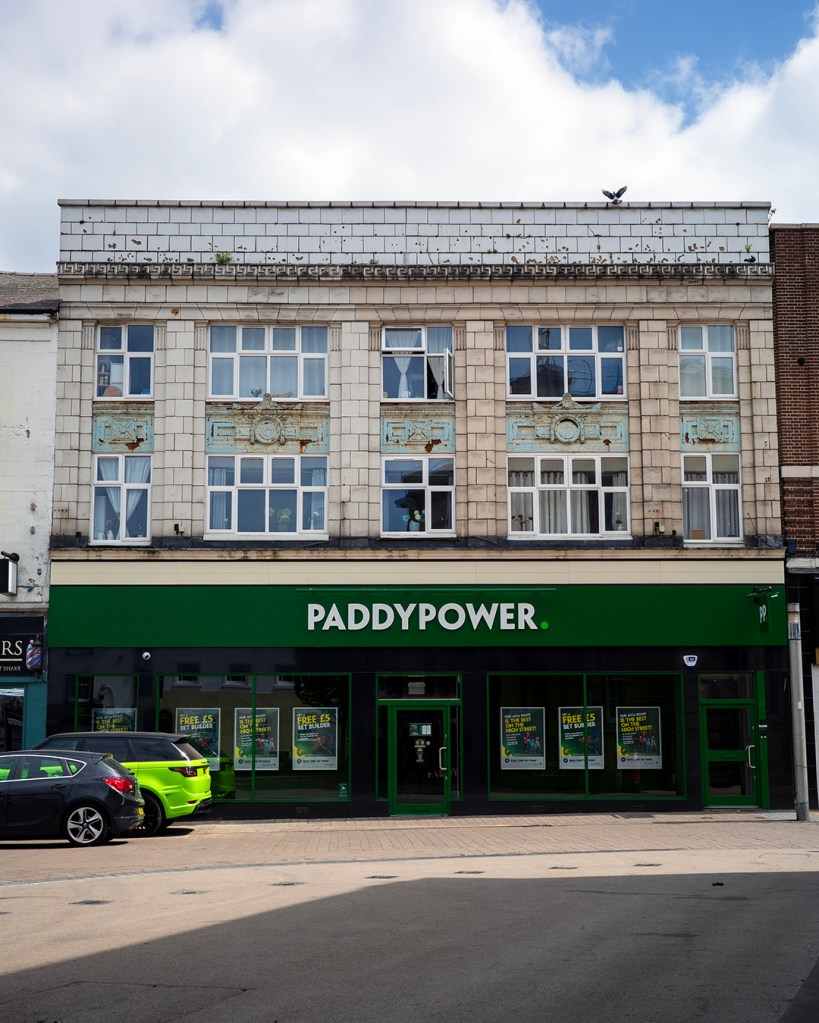 A large building with a sign reading: Paddypower and two cars parked in front of it.