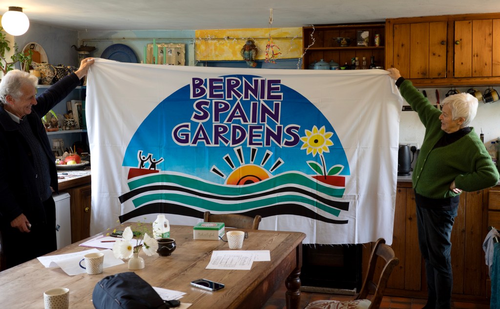 Two people hold a colourful illustrated banner with the words 'Bernie Spain Gardens'