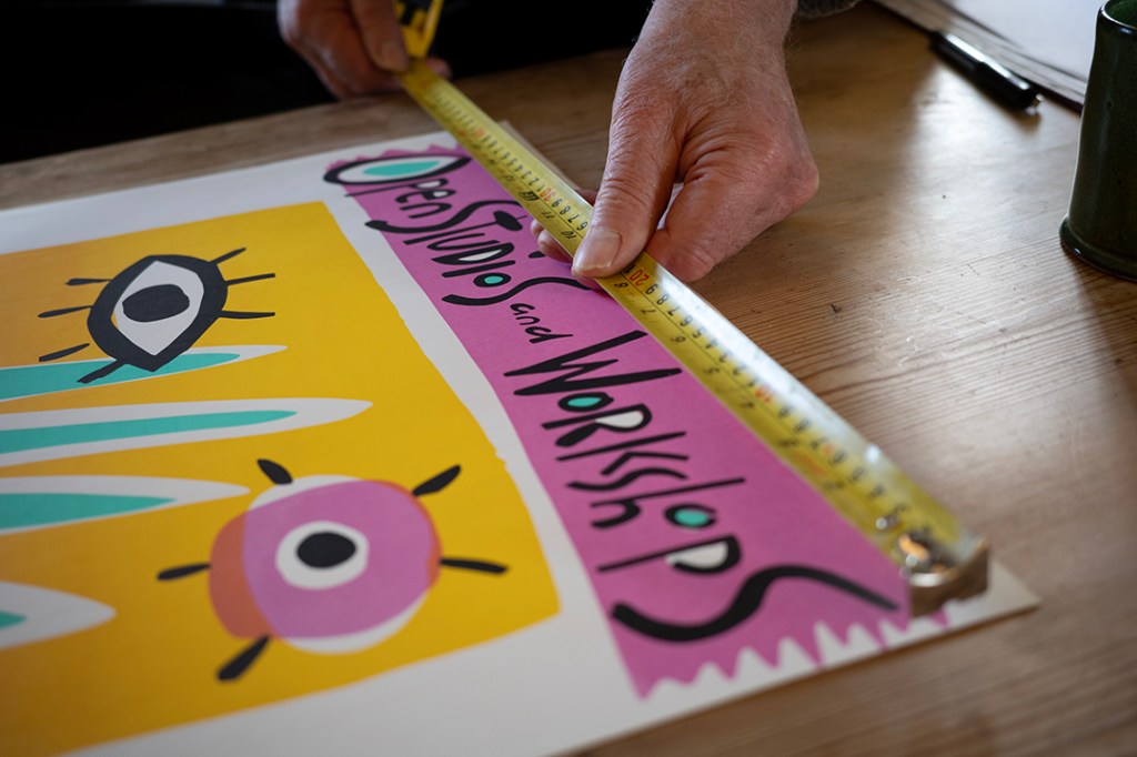 Someone measures the width of an illustrated poster with a measuring tape.