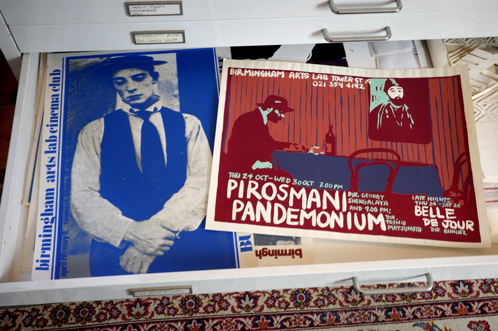 Two posters one with a man standing in blue, the other with a man sitting at a table in red.