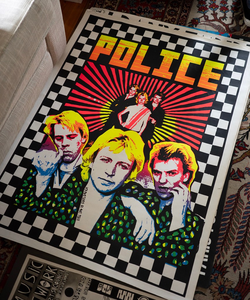 A poster with black and white checks around the edges, the word POLICE large at the top, and three people pictured twice, the first time standing in the distance, the second close up at the bottom.