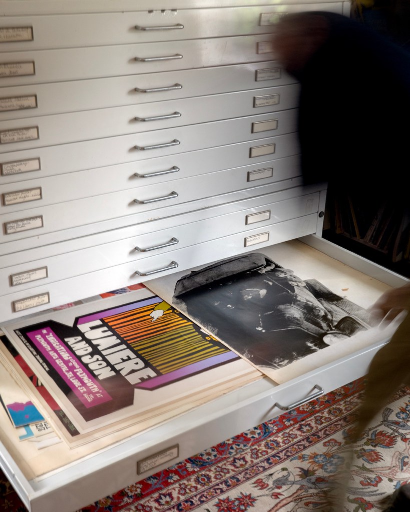 a set of draws with a blurred figure to the right bent over two posters in a pulled out draw.
